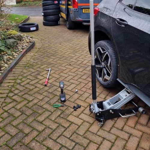Black car tyre fitting with tools and jack in
place